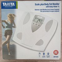 Box image showing Tanita Scale Plus Body Fat Monitor brand and model UM-081, with illustration of scale and woman running.
