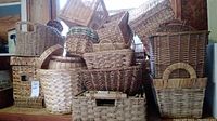 Various wicker baskets stacked and grouped, including rectangular, oval, and round shapes with handles and lids.