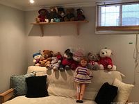 Photo of sofa with 31 inch doll in front and variety of teddy bears arranged on backrest couch and shelf above