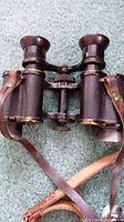 Vintage Hensoldt binoculars with leather strap on blue carpet.