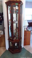 Full view of tall wood curio cabinet with glass display shelves inside and mirror back panel, standing upright in a room corner.