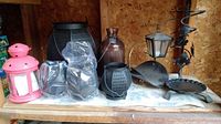 Photo shows an assortment of candle lanterns including pink metal lantern, black IKEA Rotera tealight lanterns with tags, black Nate Berkus lantern, large brown glass vase, and a small black metal lantern.