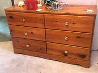 Full front view of the wood dresser showing six drawers and two columns, white round knobs, natural wood finish.