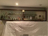 Long view of multiple drinking glasses, wine glasses, brandy sifters, empty collector bottles arranged in a display cabinet, showing the diversity of shapes and sizes.