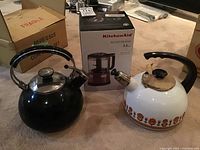 Two enamelled kettles and KitchenAid mini food processor box shown together on carpeted floor.