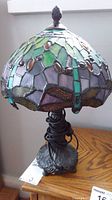 Full view of 14 inch stained glass shade on lamp with green, purple, and amber glass pieces and dark metal base.