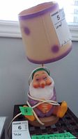 Full view of Sleepy lamp showing dwarf figurine base, beige and purple lampshade, and power cord wound around the base.