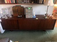 Full view of the Mid-Century Modern sideboard cabinet showing three sliding doors and top surface with various objects.