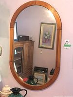 Oval wood frame mirror hanging on a wall, clear reflection visible.