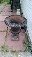 Front view of cast iron planter placed on outdoor paving, showing rust inside and ornate rim
