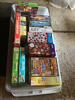 Full view of over 17 jigsaw puzzle boxes stacked in a plastic bin showing various themes and brands