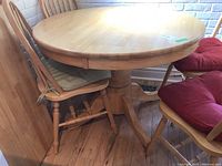 Wooden round dining table with chairs around and visible extension split in the center.