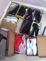 Top down view of nine pairs of women's shoes mostly in boxes, shows mix of dress and casual sneakers