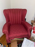 Front view of the red upholstered wingback armchair showing patterned fabric and wooden legs.