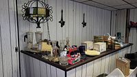 Wide shot of basement bar counter displaying multiple items including the Oster blender, decanter, glass stemware, and Coca-Cola collectibles.