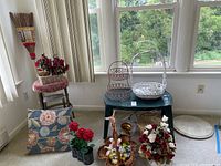 Overview of lot showing decorative pillow, faux flowers, wire baskets, electric candles, plastic table, small stool with floral cushion, and marble table top on the right side.