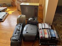 Full view showing heaters (Wards and Pelonis), Sony CFD-S70 CD radio cassette player, Lenox AM/FM cassette radio, GPX TV radio, and stacked CDs and cassettes in labeled case