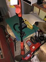 Photo showing the Grass Hog weed whacker with orange and black handle, placed near the Homelite chainsaw.