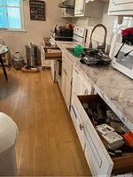 Wide view of kitchen drawers partially open showing assortment of kitchen utensils, tools, and other items inside three drawers.
