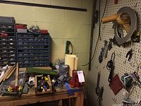 View of tool bench with various tools and plastic bins, pegboard with hanging hand tools including pliers, wrenches, clamps, pulley, chisels, hand saws, and assorted hardware items.