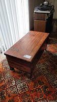 View of entire wooden Lane chest showing rectangular shape, hinged lid with metal strap hinges, scratches on wood surface, and vintage-style carpet beneath.
