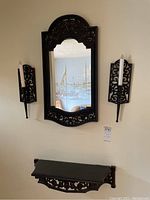Full view of mirror, both sconces, and shelf mounted on the wall showing ornate black plastic design and items grouped together.
