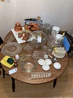 Full table overview showing clear glass items, copper molds, and some kitchenware on a round wooden table.