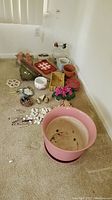 Wide shot of lot showing large pink pot, smaller terracotta pots, green hanging planter, artificial pink flowers, angels on bench, wind chimes and other decorative items all placed on floor near corner