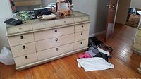 Full view of dresser with assorted shoes on floor and various handbags and jewelry on top of dresser.