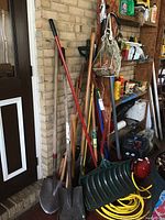 View of shovels, broom, axe, extension cord, and other tools leaning against wall and shelf