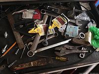 Top view of toolbox drawer with assorted wrenches, pliers, socket tool attachments, screwdrivers, and utility knife showing arrangement of mixed hand tools.
