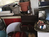 Photo showing the large brown metal toolbox open with a smaller red metal toolbox inside. Behind and beside are canvas pouch, plastic potting pots and gas cans.