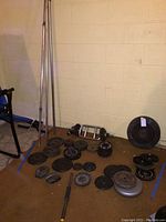 Wide angle showing full set of weights and barbells arranged on floor against a wall in a basement.