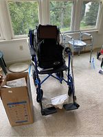 Blue aluminum wheelchair with attached bags and Vitalwrap box beside