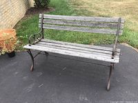 Front-side angle view of the outdoor bench showing wood slats and rusted iron base with armrests.