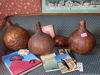 Three large Kenyan etched gourds displayed on a patterned blue sofa with six African-themed books including Maasai warrior and Serengeti publications.