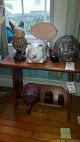 Wide shot of a table displaying several animal figurines including two rabbits, three pigs (one wooden, one white ceramic, one pig bookend set), and a small black bird figurine.