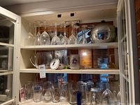 Wide angle shot of the barware collection including stemmed glasses, pitcher, coasters, various drinking glasses, glass mug, and penguin ice bucket on shelves.
