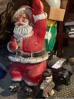 Photo showing vintage blow mold Santa seated with raised hand, alongside Bobs Big Boy rubber toy and Scottie dog figurine on carpeted floor.