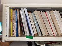 Photo showing a side view of 18 cookbooks with titles visible such as The French Laundry Cookbook, Waverley Root Food Encyclopedia, Moscow Cookbook, and more.