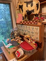 Photo showing large cow figurine, pink pig wall art, small wall cabinet with herbs and farm animals design, decorative skewers, and other smaller items.