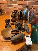 Photo showing wood animal figures including pig, horse, cat, and a tiger figure. Several round and paddle wooden cutting boards. Russian metal coffee pot with black Bakelite handle and knob. Stacked wooden bowls. Black Crock Stick sharpener. Metal cookie cutters visible.