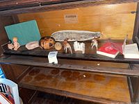 Shelf view with figurines including ceramic pig, carved wooden fish, plastic deer, dolls, and books