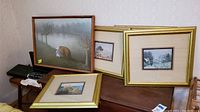 Four framed art prints shown together on a wooden surface, one prominently featuring a girl and two bears near a lake, all frames dusty and in need of cleaning