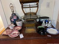 Wide view of the vintage lamp, transferware dishes, blue stoneware, Beleek shell, salt and pepper shakers, and Flow Blue plate on wooden surface.