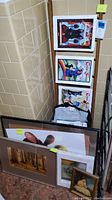Photo showing several framed prints leaning against a wall and ladder, featuring abstract and animal-themed artwork.