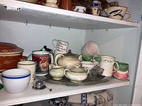 Shelf with a variety of mugs including novelty animal mugs and a Steubenville tea set with teapot, sugar bowl, creamer, and tray.