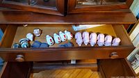 Drawer with multiple ceramic napkin rings shaped like white chickens, pink pigs, and blue patterned rings arranged in rows.