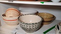 Shelf display featuring vintage pottery bowls with various stripes and speckled patterns arranged in stacks.