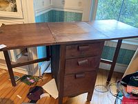 Full view of vintage wooden gate-leg desk with both sides folded down, showing surface scratches and wear on the top.